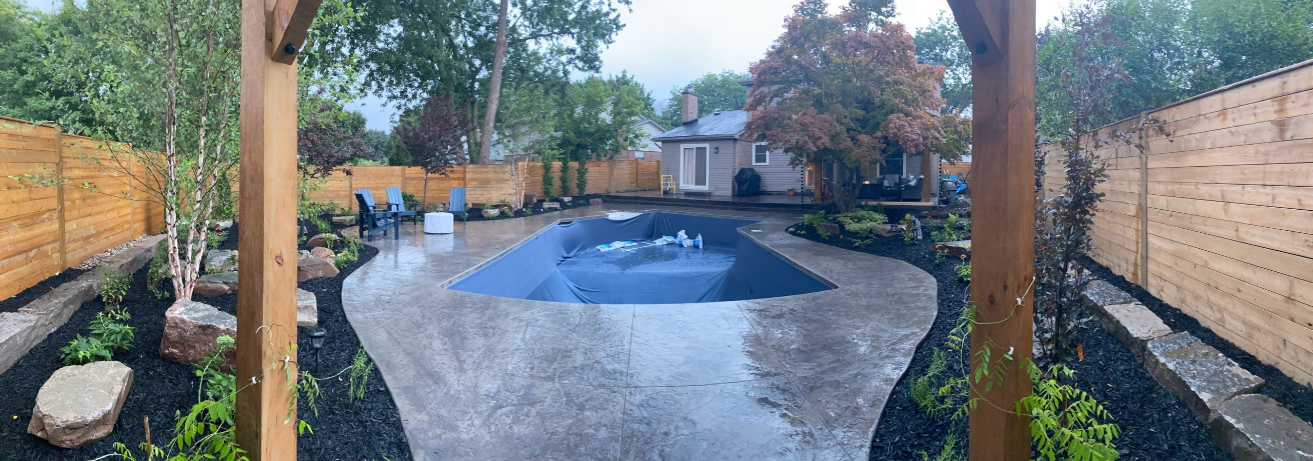 after photo of new backyard with refurbished pool, concrete deck, shade structures, patio, gardens