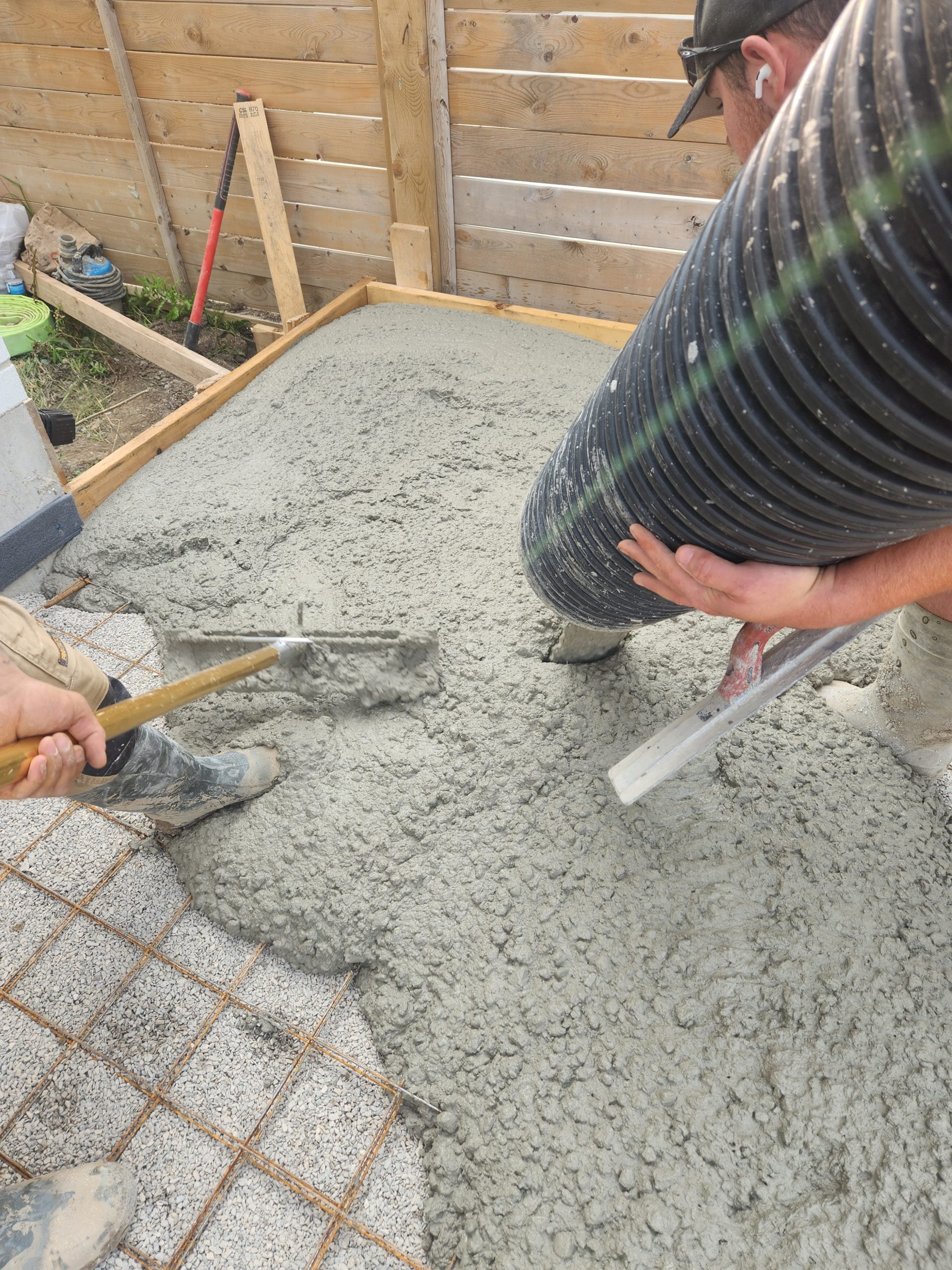 close up of concrete delivery for pool deck surrounding inground pool - one worker guiding fresh concrete while another pushes it to evenly spread in desired sections