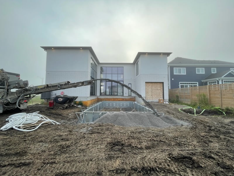 slinger throwing gravel around steel pool panels, footings and plumbing for backfill