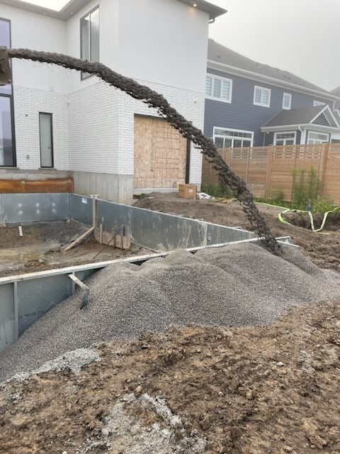 slinger throwing gravel around steel pool panels, footings and plumbing for backfill
